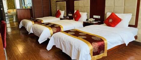 A hotel room with three beds, each with a red and gold bedspread, wooden headboards, and a wooden floor.