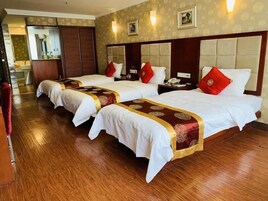 A hotel room with three beds, each with a red and gold bedspread, wooden headboards, and a wooden floor.