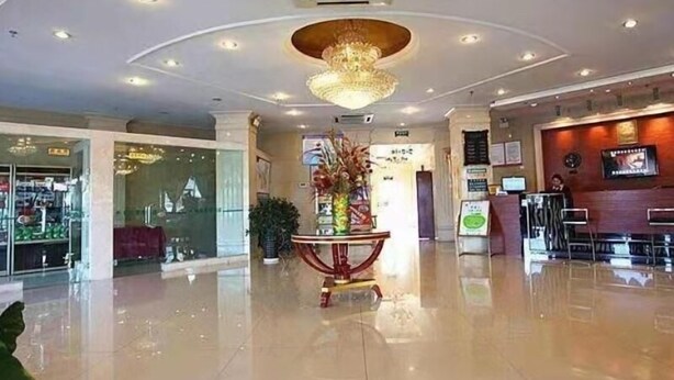 A hotel lobby with a polished floor, a central decorative plant, and a chandelier.