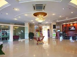 A hotel lobby with a polished floor, a central decorative plant, and a chandelier.