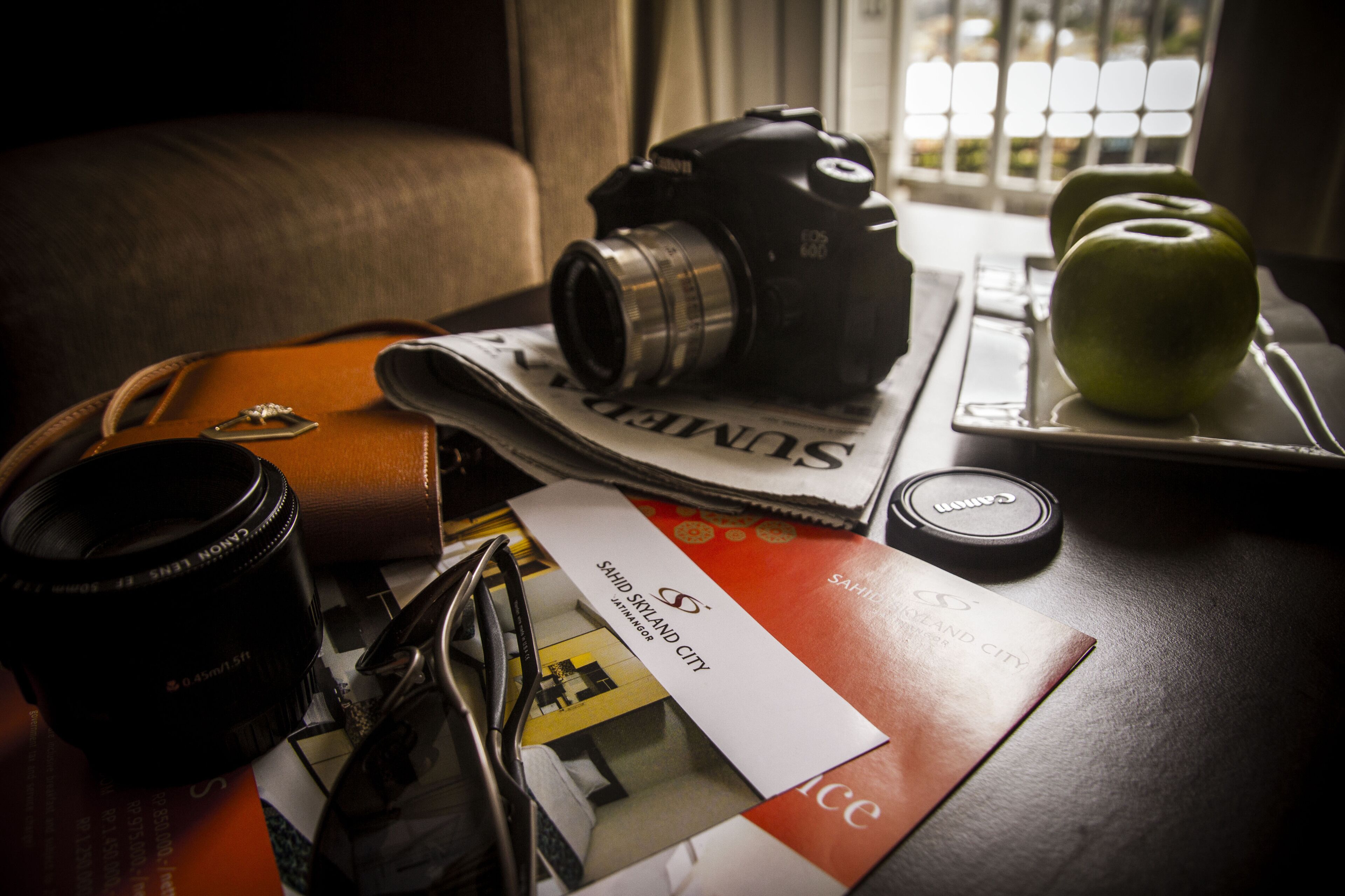 A camera, a pair of glasses, a wallet, and a tray with apples on a table.