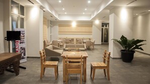 A spacious lobby with a wooden table and chairs, a sofa, and a large potted plant. - Sahid Skyland City Jatinangor Hotel (Hegarmanah)