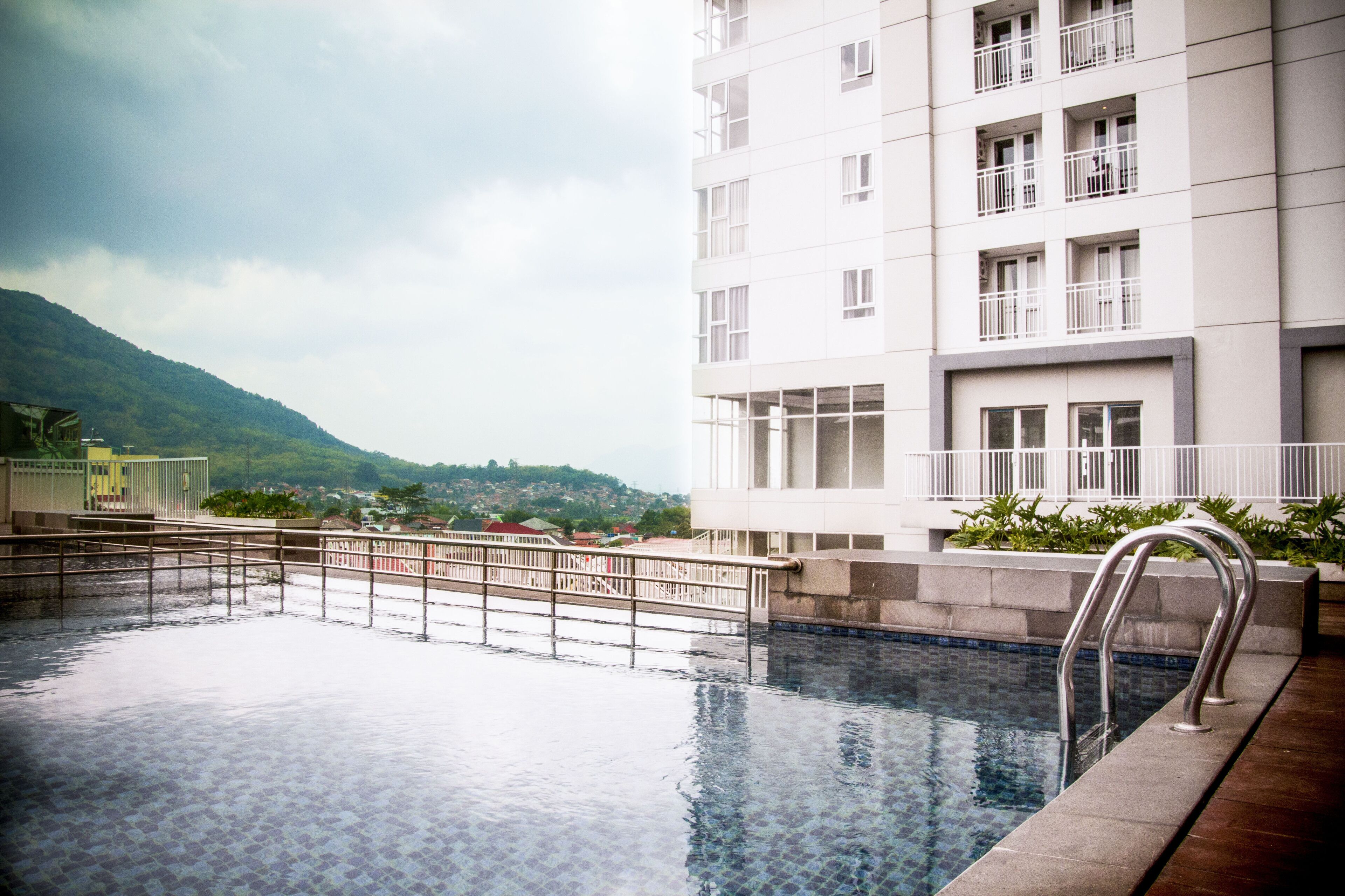 Una piscina con escalera metálica, rodeada por una terraza con baldosas.