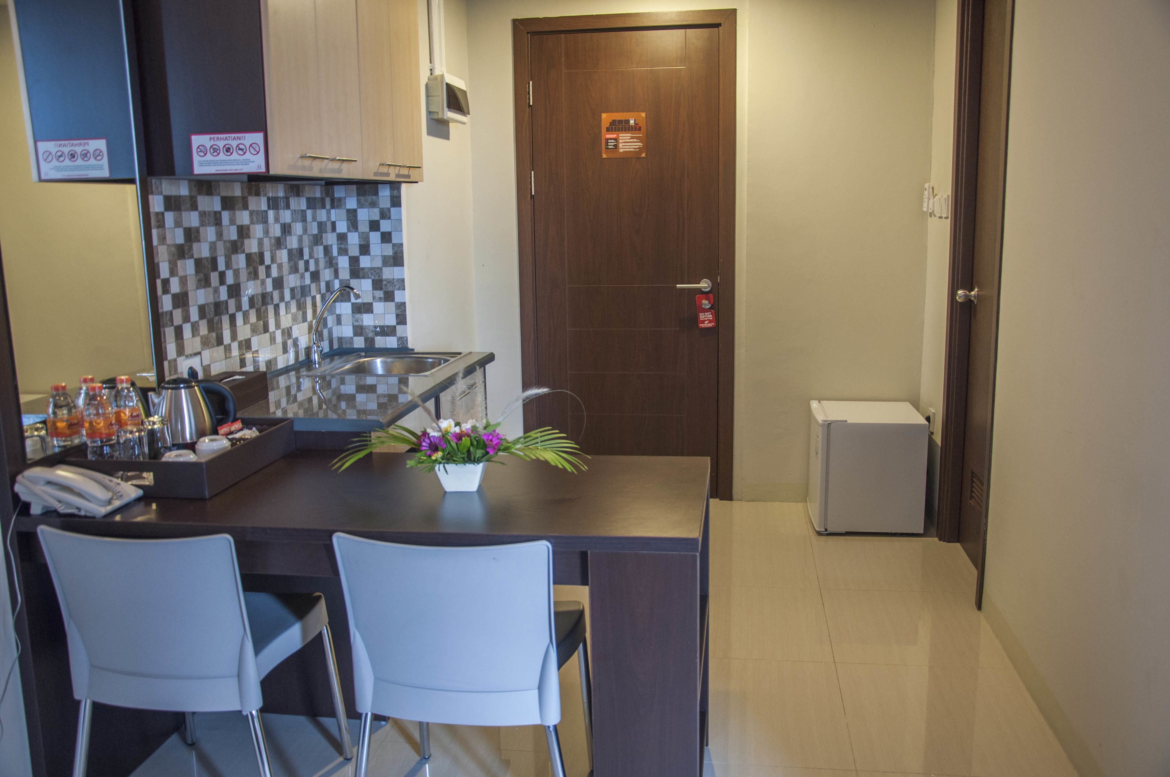 A small kitchen with a checkered backsplash, a sink, a refrigerator, and two white chairs.