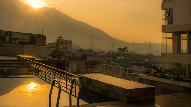 A rooftop terrace with a wooden deck, a metal railing, and a view of a cityscape with mountains in the background. - Sahid Skyland City Jatinangor Hotel (Hegarmanah)