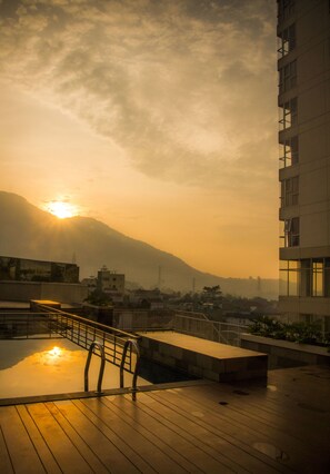A rooftop terrace with a wooden deck, a metal railing, and a view of a cityscape with mountains in the background. - Sahid Skyland City Jatinangor Hotel (Hegarmanah)