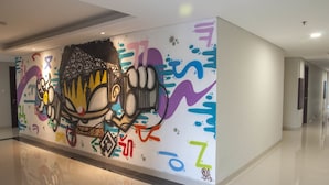 A hallway with a colorful graffiti mural on the wall, a polished floor, and a door at the end. - Sahid Skyland City Jatinangor Hotel (Hegarmanah)