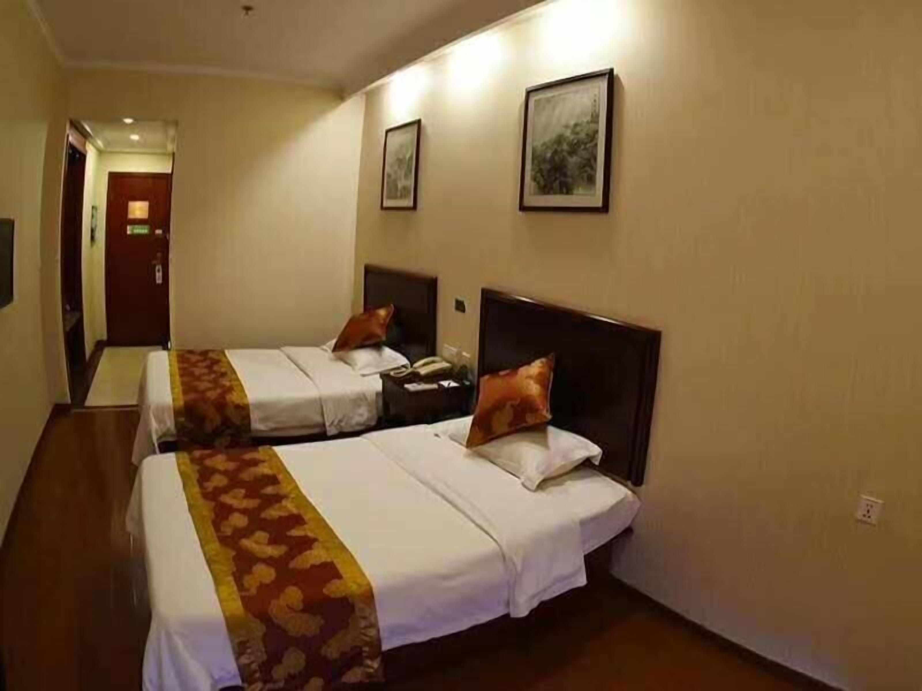 A hotel room with two beds, each with a headboard, a bedside table, and a lamp. There is a door leading to another room and a wall-mounted picture.