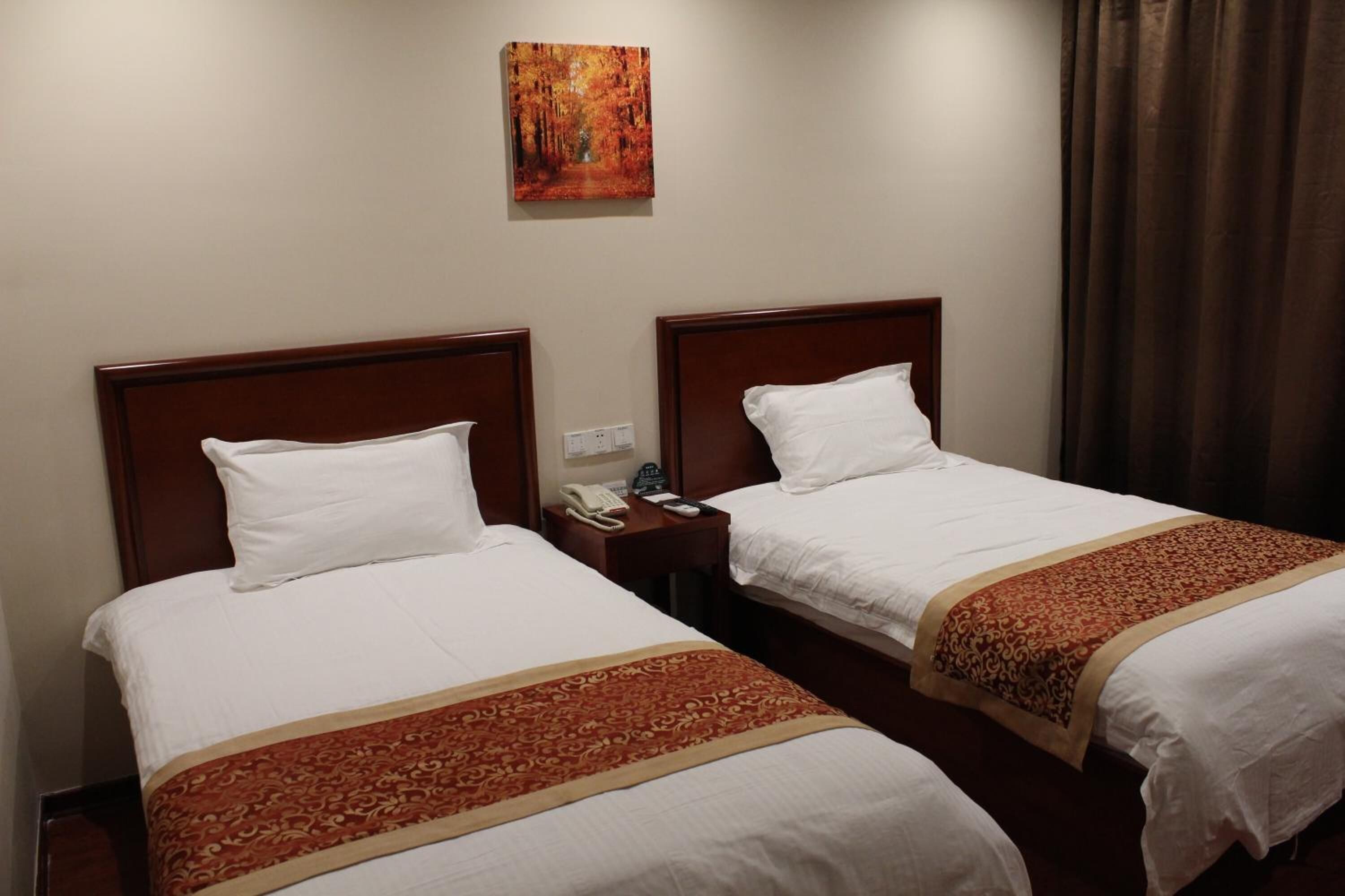 Habitación de hotel con dos camas, cada una con cabecero de madera, ropa de cama blanca y colcha estampada de color rojo. Se observa un teléfono y un enchufe en la mesita de noche entre las camas.