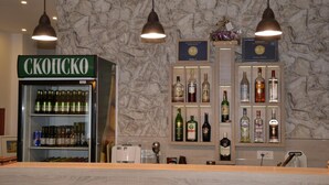 A bar area with a 'SKOPISKO' refrigerator stocked with beverages, a selection of liquor bottles, and hanging pendant lights. - Villa Arte (Ohrid)