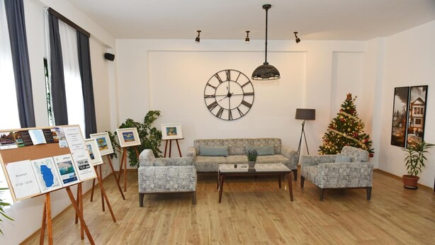 A living room with a sofa set, a coffee table, a wall clock, a Christmas tree, and a display of framed pictures. - Villa Arte (Ohrid)