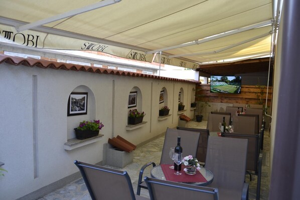 An outdoor patio with tables and chairs, a TV screen, and a sign with the word "STORI". - Villa Arte (Ohrid)