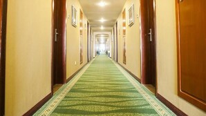 Un pasillo de hotel con puertas a ambos lados, alfombra verde e iluminación empotrada en el techo.