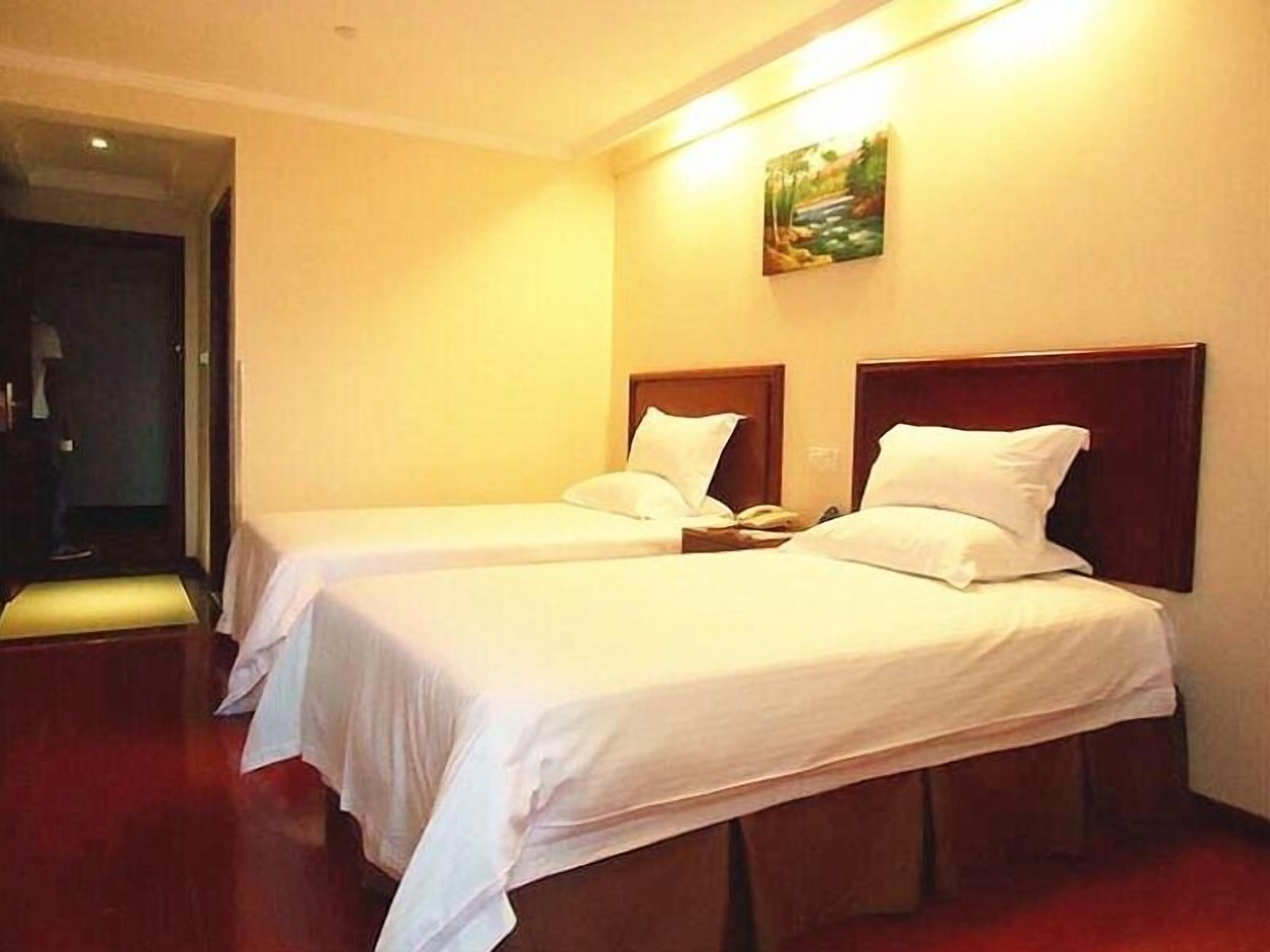 A hotel room with two single beds, a wooden headboard, and a painting on the wall.