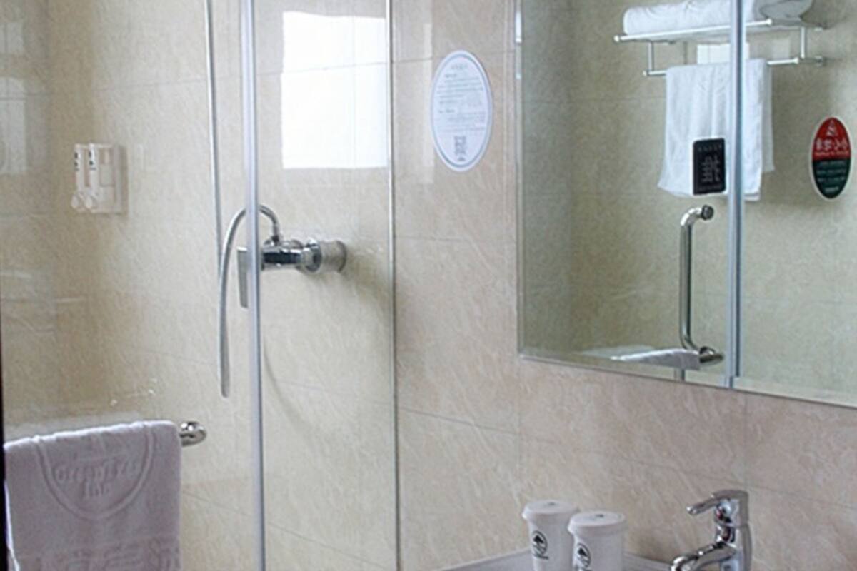 Ein Badezimmer mit Duschabtrennung aus Glas, einem Handtuchhalter und einem Spiegel, der ein Handtuch und eine Seifenspender reflektiert.