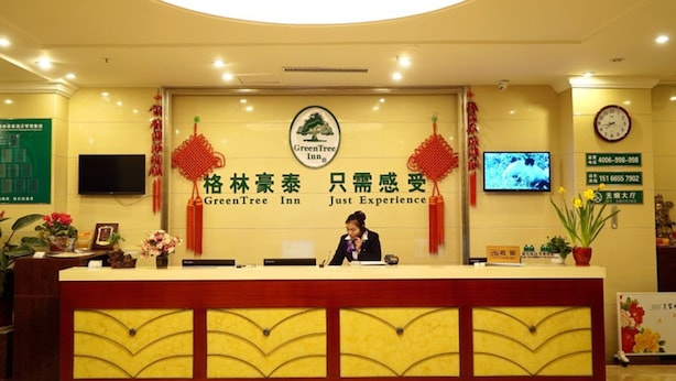 A hotel reception desk with a sign for GreenTree Inn and a clock on the wall. - GreenTree Inn Liaocheng Town Dongchang Road Zhuanpan Business Hotel (Liaocheng)