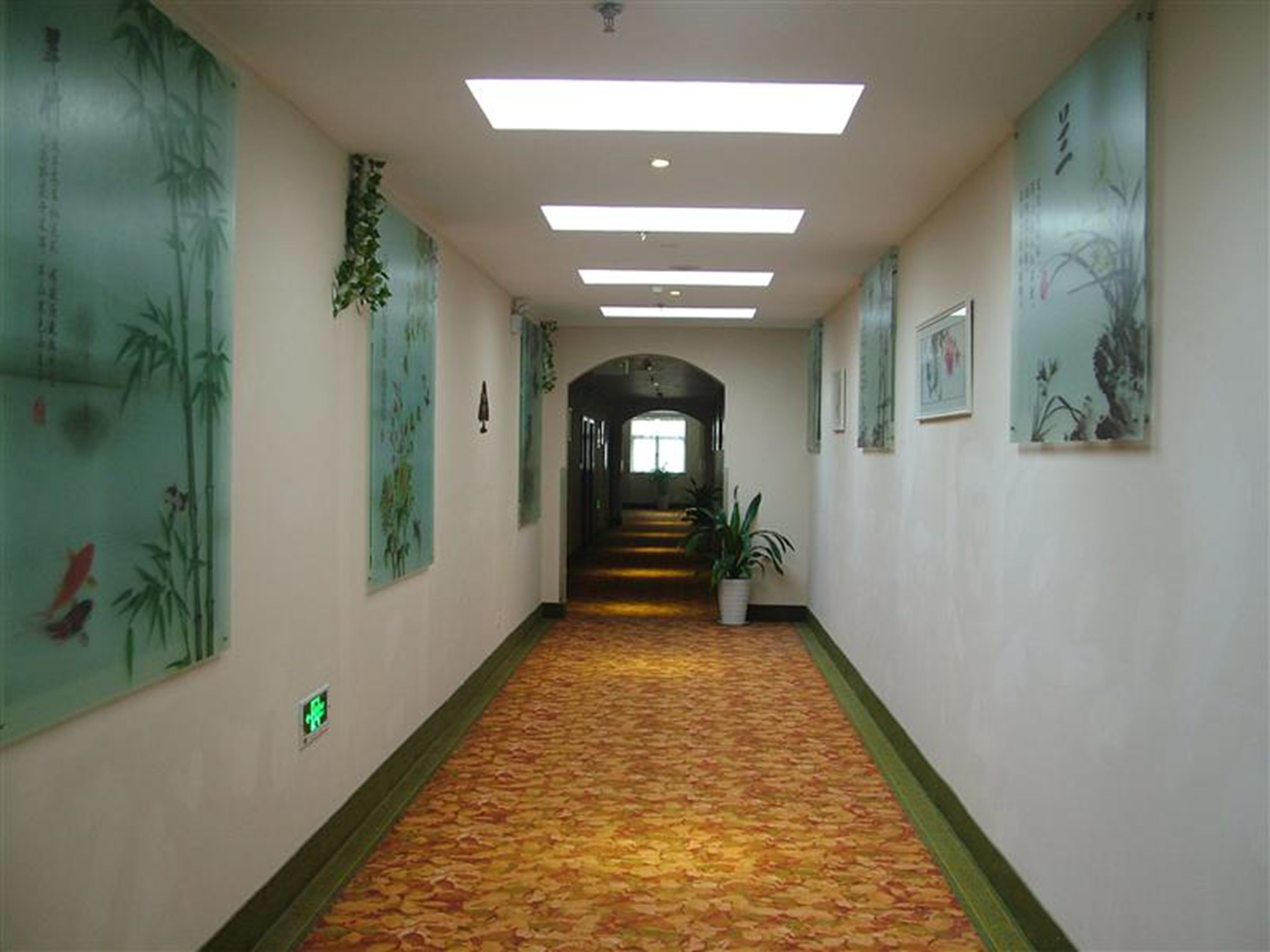A hallway with a patterned carpet, green wall decorations, and a staircase leading to another level.