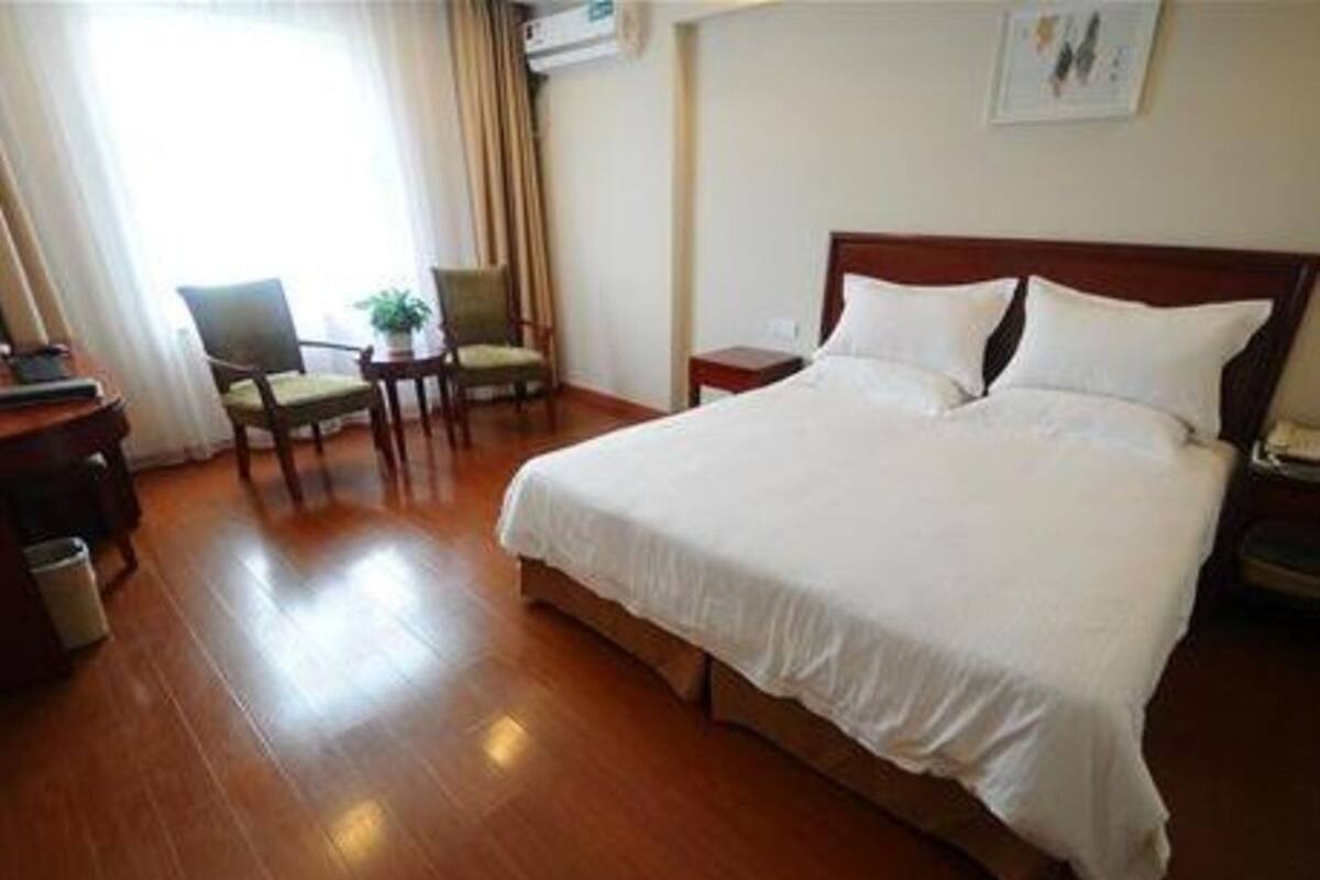 A hotel room with a large bed, a bedside table, a chair, and a small table with a plant.