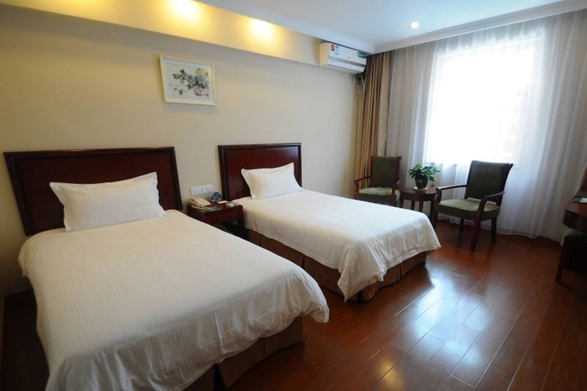 A hotel room with two beds, a nightstand, a chair, a small table, and a potted plant.