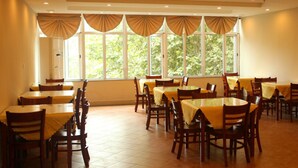 A dining area with multiple tables and chairs, large windows with curtains, and a tiled floor. - GreenTree Inn Huaian West Huaihai Road Hotel (Huai'an)