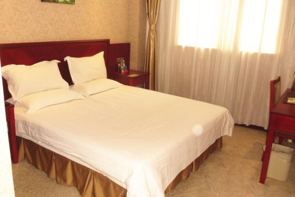 A hotel room with a large bed, a nightstand, a desk, and a window with curtains.