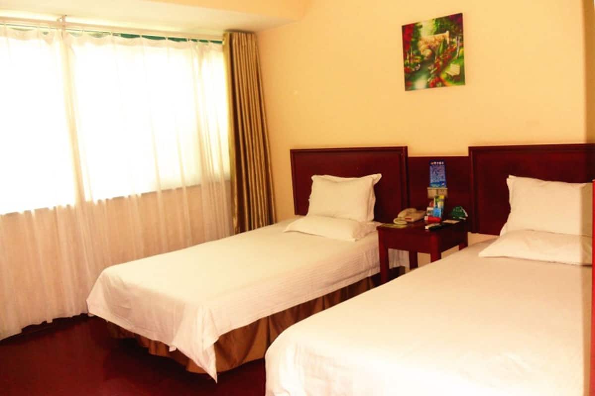 A hotel room with two single beds, a wooden headboard, a nightstand with a phone and a lamp, and a painting on the wall.