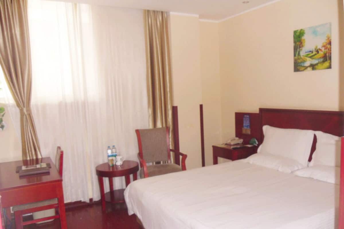 A hotel room with a bed, a desk with a chair, a small table with a chair, and a painting on the wall.