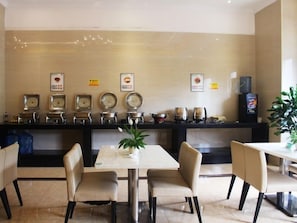 Un restaurante con un mostrador que exhibe diferentes platos, una mesa con sillas y una planta en maceta.