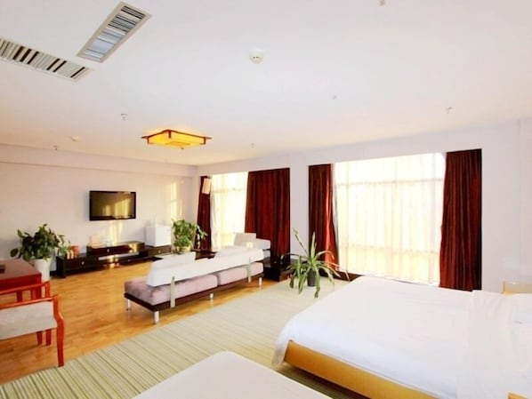 A hotel room with a bed, a sofa, a TV, a desk, and a window with curtains.