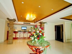 A hotel lobby with a reception desk, a chandelier, and a floral centerpiece on a round table.