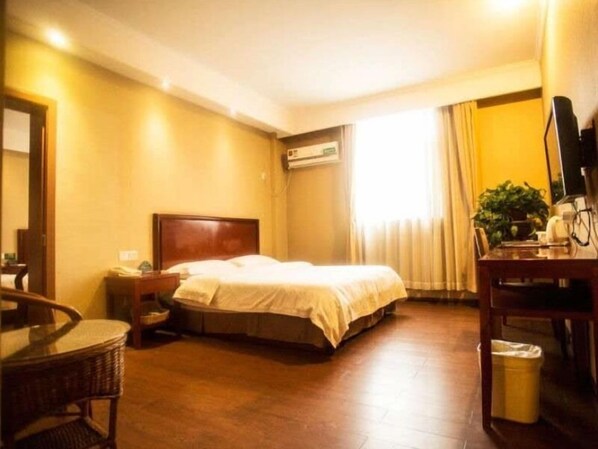 A hotel room with a bed, a desk, a chair, a trash bin, and a window with curtains.
