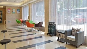 Un hall d’hôtel au design moderne, offrant différents types de sièges, notamment un canapé gris, des fauteuils colorés et un espace bar.