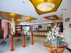 Eine Hotelhalle mit Empfangstresen, einer Chandelüster und einer Blumenkomposition.
