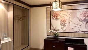 Een hotelkamer met een houten garderobe, een donker houten kast en een wanddecoratie van roze bloemen.