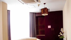 Een woonkamer met een bank, een salontafel, een decoratieve hanglamp, een donker houten deur en een potplant met witte bloemen.