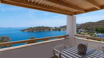 A balcony with a view of a coastal landscape, a table with a vase, and a wooden ceiling structure.