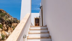 A white staircase leading to a door, surrounded by white walls, with a clear blue sky above. - Allotina Houses (Patmos)
