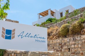 Ein Schild für Allotina Houses mit einem modernen Gebäude im Hintergrund.