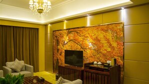 Een woonkamer met een grote flatscreen-televisie, een houten salontafel, een bank en een decoratieve wand met herfstbladeren.
