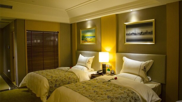 Een hotelkamer met twee bedden, een nachtkastje, een lamp en kunstwerken aan de muren.