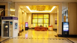 Een hotel lobby met een receptiebalie, een digitaal informatiekiosk en een geldautomaat.