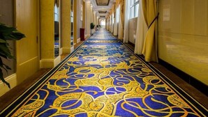 Een hotelgang met een kamerbreed tapijt met patroon, gele muren en een plafond met bloemenmotief.