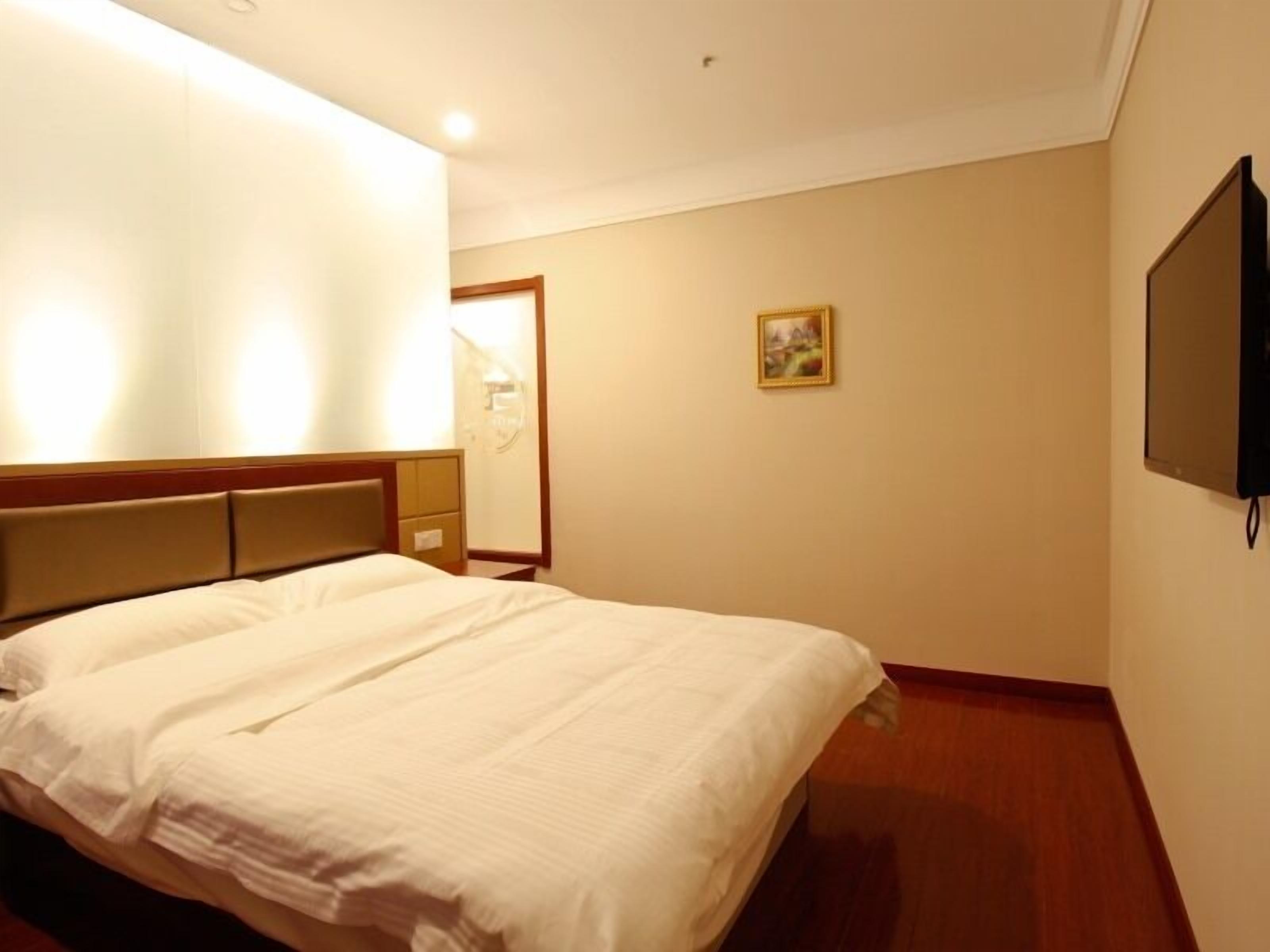 A hotel room with a large bed, a wooden headboard, a flat-screen TV mounted on the wall, and a small painting on the wall.
