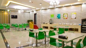 A spacious dining area with green chairs and tables, a chandelier, and a counter with a cash register.