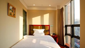 A hotel room with a large bed, a bedside table, a nightstand, a window with curtains, and a painting on the wall.