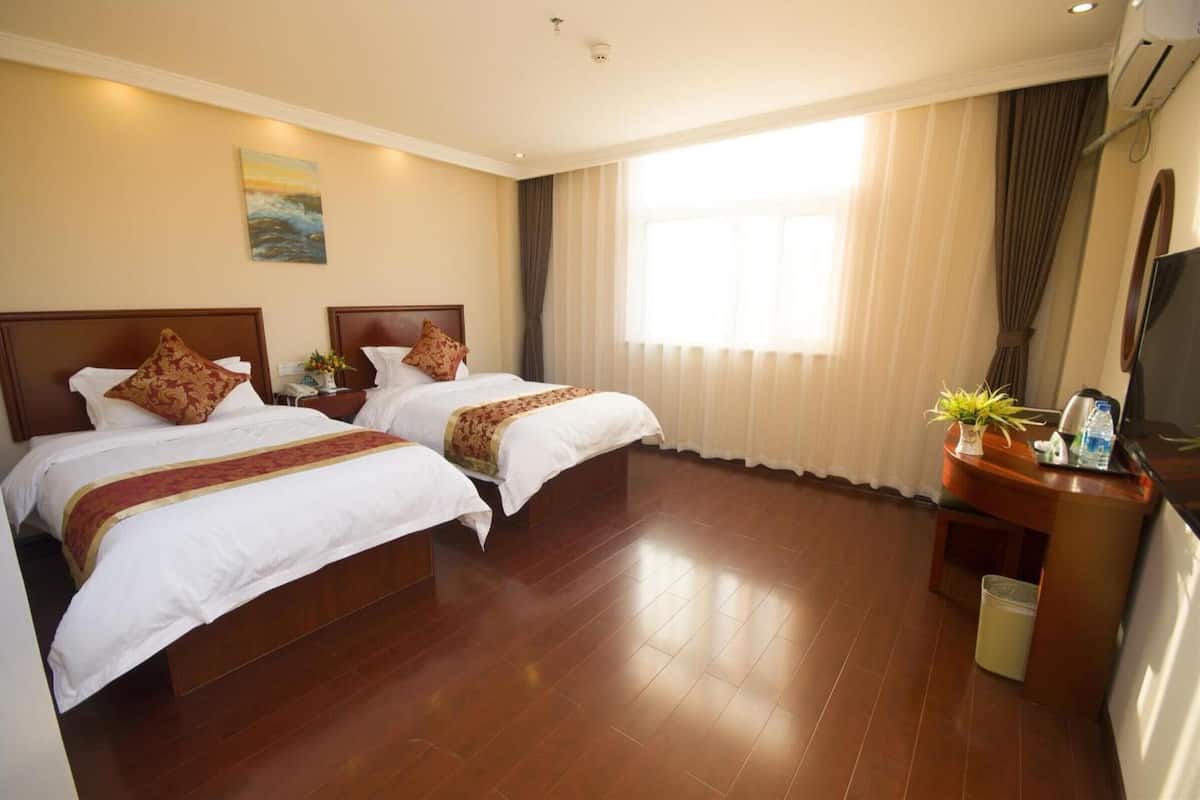 A hotel room with two beds, a desk with a TV, and a large window with curtains.