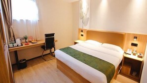 Une chambre d’hôtel avec un lit, un bureau, une chaise et une petite poubelle.