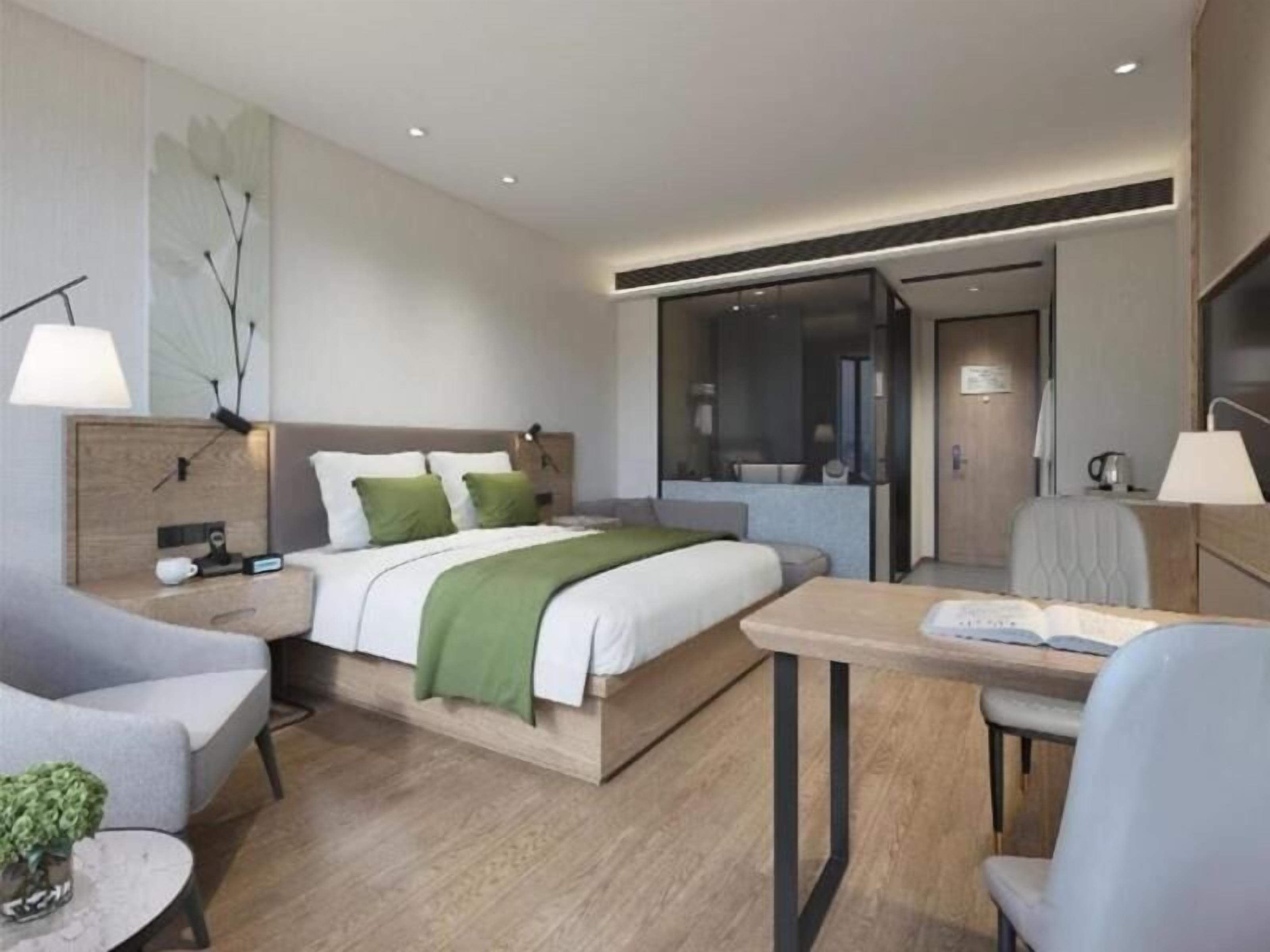 A modern hotel room with a bed, bedside tables, a desk, and a chair.