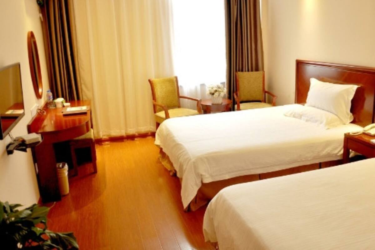 A hotel room with two beds, a desk, a chair, and a small table with a vase of flowers.