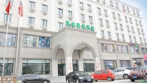 Un hôtel à plusieurs étages, doté d’une façade blanche, de nombreuses fenêtres et d’une enseigne verte au-dessus de l’entrée.